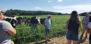 Collaborating farmer, Ron Schoepp, discusses rotational grazing in front of an audience at a field event on his farm. Cattle and lush pasture vegetation is in the background.