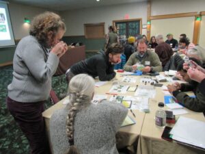 Conference participants are participating in a hands on activity, looking at identifying pictures for pests, some looking through small handheld magnifying lenses.