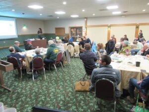 A conference room full of people seated at tables looking at a presentation.