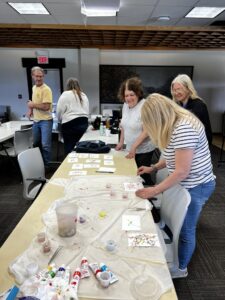 people around a table using paint-dipped maggots to paint on blank postcards