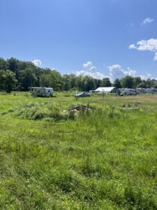 grassy field with burn pit and greenhouse, RV and car in the background