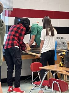 Students engage in hands-on learning, using tools to measure and cut wood planks as part of a classroom design and technology project to build a vertical garden.