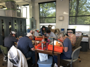 A picture of a room with several people seated at tables at a honey bee workshop.