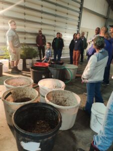 Workshop participants and facilitator stand near tubs of materials that will make a compost pile