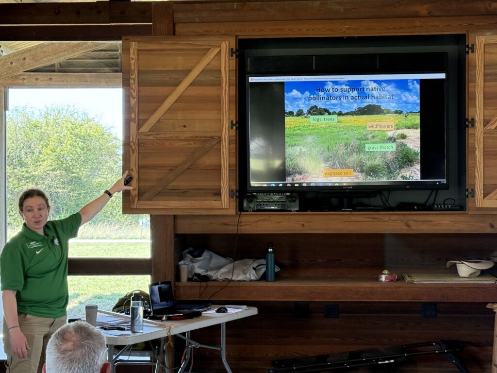 Photograph showing a slide about pollinator habitat and a person pointing at the slide while talking to an audience
