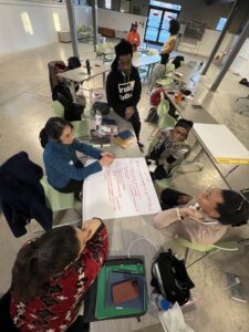 A group of people sit at a table over a sheet with the heading "PITCH"