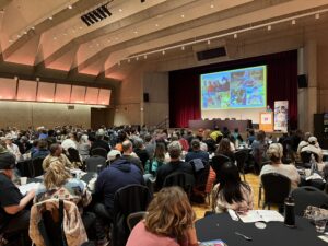 Hundreds of people sitting watching a conference slide show