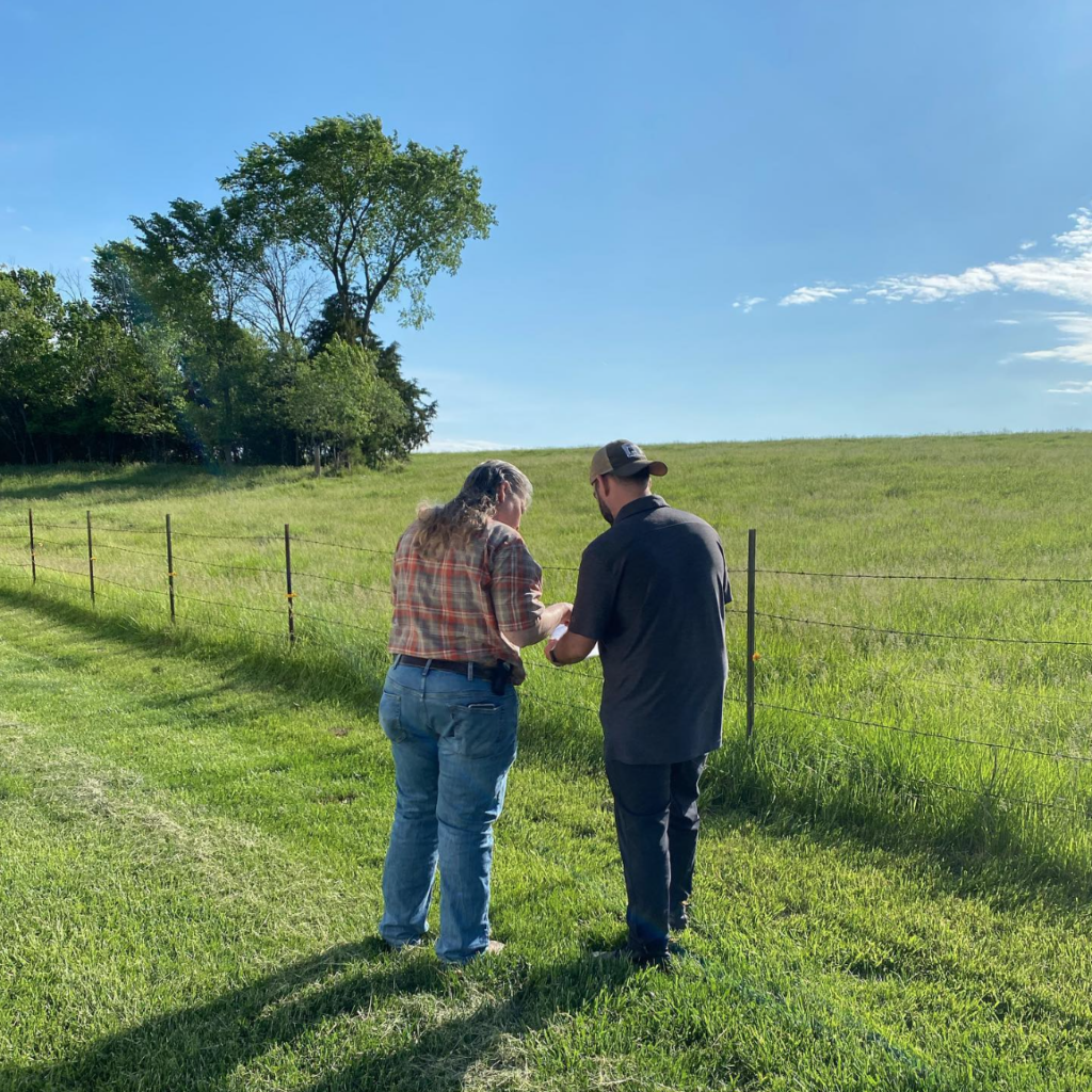 A woman and a man stand in front of a pasture reading a document