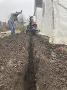Photo shows a trenching machine and the narrow trench it created. Also visible is a section of stone and brick along one edge of the trench.