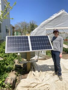 Photo shows graduate student JT alongside the solar panel installed to provided power to the system's fan