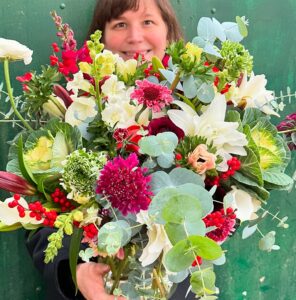 Farmer Rebecca Kutzer-Rice holding mixed arrangement of December cut flowers including lilies, snapdragons, and anemones.