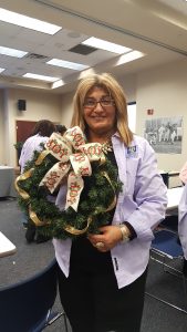 An instructor at SU 2016 Fall Garden Workshop proudly holds a finished holiday wreath with large bow.