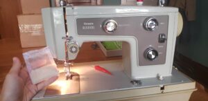 Photo of a sewing machine with a hand holding a small nylon mesh packet.