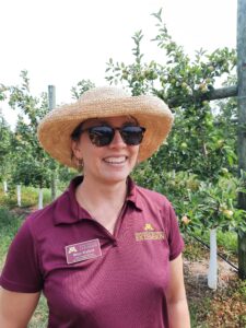 Women in straw hat, sunglasses smiling in front of apple trellis