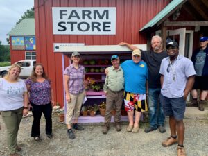 CFN staff visit Prospect Meadow Farm at Service Net.  Seven people standing in front of red barn with sign "Farm Store"