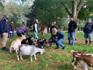 Farmers on a tour of OASIS in New Jersey.  Farmers are petting cute baby goats (some white, black & white spekcled color and brown)