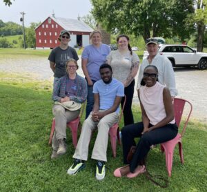 Red Wiggler Farm hosts 7 beginning farmers for a farm tour. people are posing in a line in front of a red barn.