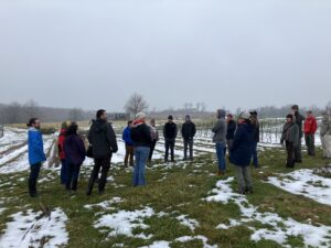 15 farmers staninding in circle at Red Wiggler Care Farm.  They are standing in a snow covered path looking at the vegetable beds covered in snow.