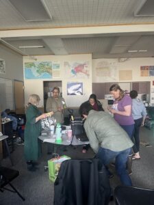 Workshop attendees gather around a table inside of a classroom, assembling soil, containers and saran wrap for indoor seed starting.