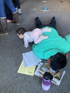 A baby crawls over a boy reading agricultural pamphlets on the ground